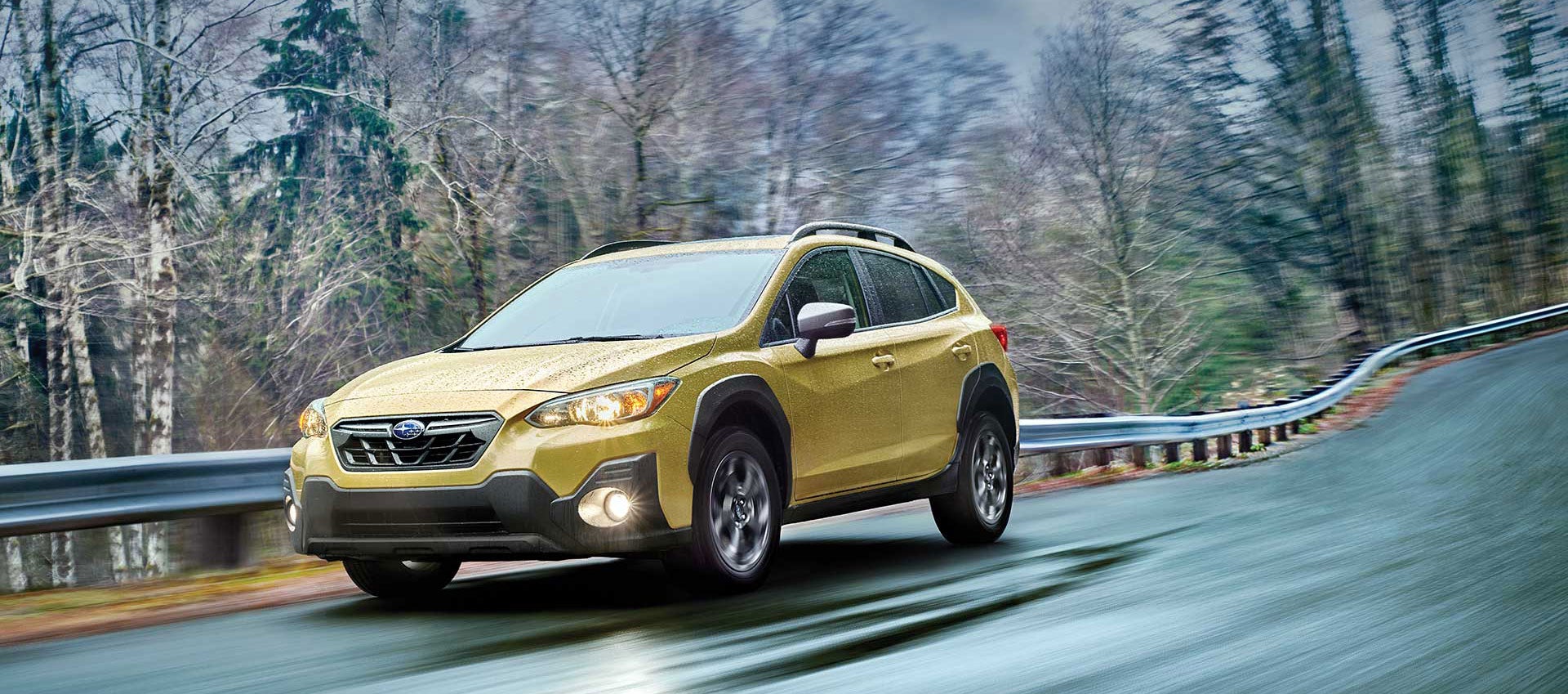 Gold Subaru Crosstrek driving fast on a wet, winding road through a forest