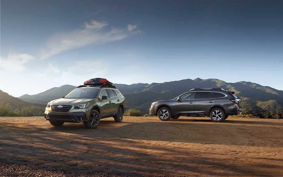 Two Subaru Outback vehicles parked on a dirt overlook with mountain scenery in the background