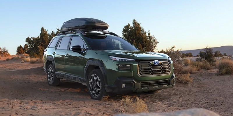 Green Subaru SUV with rooftop cargo box parked in a desert setting