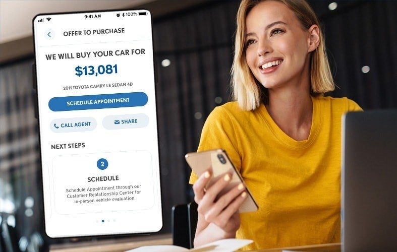 Smiling woman looking at a phone showing a $13,081 car purchase offer for a 2011 Toyota Camry