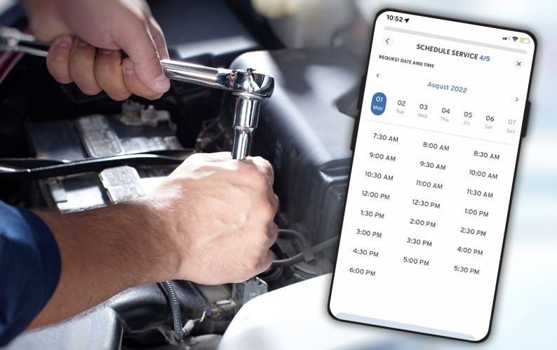 Mechanic working on a car engine, with a smartphone displaying an app to schedule service appointments for August 2022